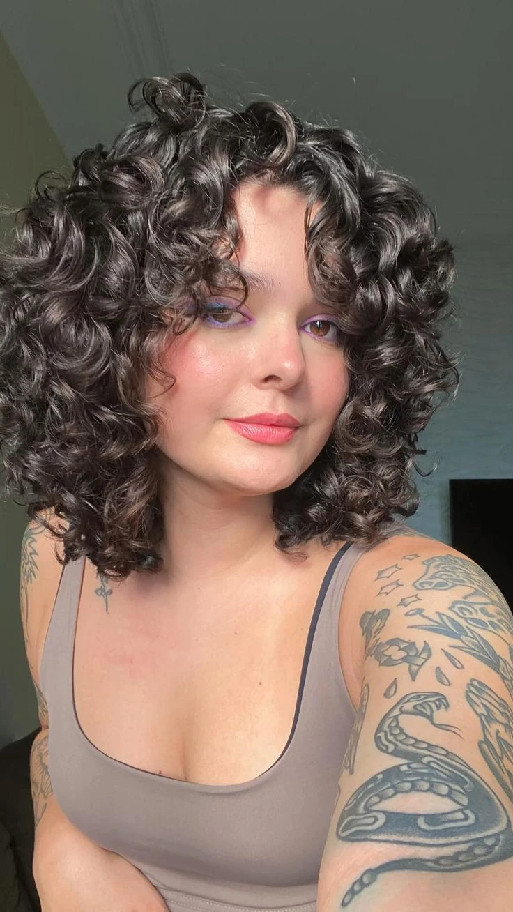 Mulher com cabelo cacheado estilo shaggy hair, corte despojado e volumoso que realça os cachos naturais.