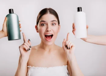 Mulher escolhendo entre dois shampoos, um verde e outro branco, com expressão de surpresa e empolgação.