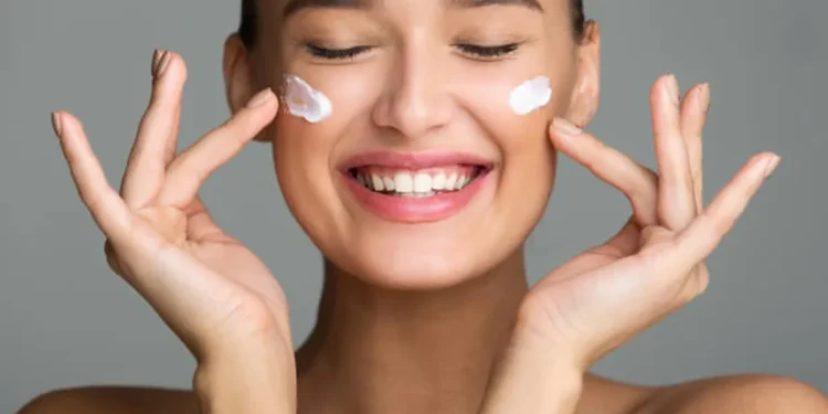 Cuidados com a pele: aprenda a rotina ideal para o seu tipo de pele! 1 Mulher sorrindo aplicando creme facial em sua pele, representando uma rotina de cuidados com a pele.