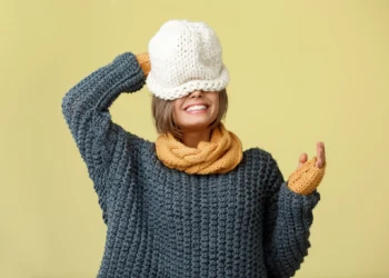 Mulher sorrindo e usando um conjunto de tricô quente com cachecol e luvas amarelas, com chapéu branco, destacando tendências de moda para o inverno.