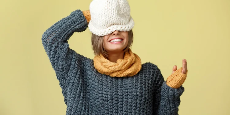 Descubra as tendências de moda da temporada: o que está em alta agora? 1 Mulher sorrindo e usando um conjunto de tricô quente com cachecol e luvas amarelas, com chapéu branco, destacando tendências de moda para o inverno.