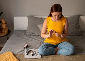 Mulher fazendo as unhas em casa com kit de manicure ao lado