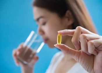 Pessoa segurando cápsula de vitamina D com um copo de água, destacando o momento de tomar suplemento.