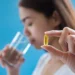 Pessoa segurando cápsula de vitamina D com um copo de água, destacando o momento de tomar suplemento.