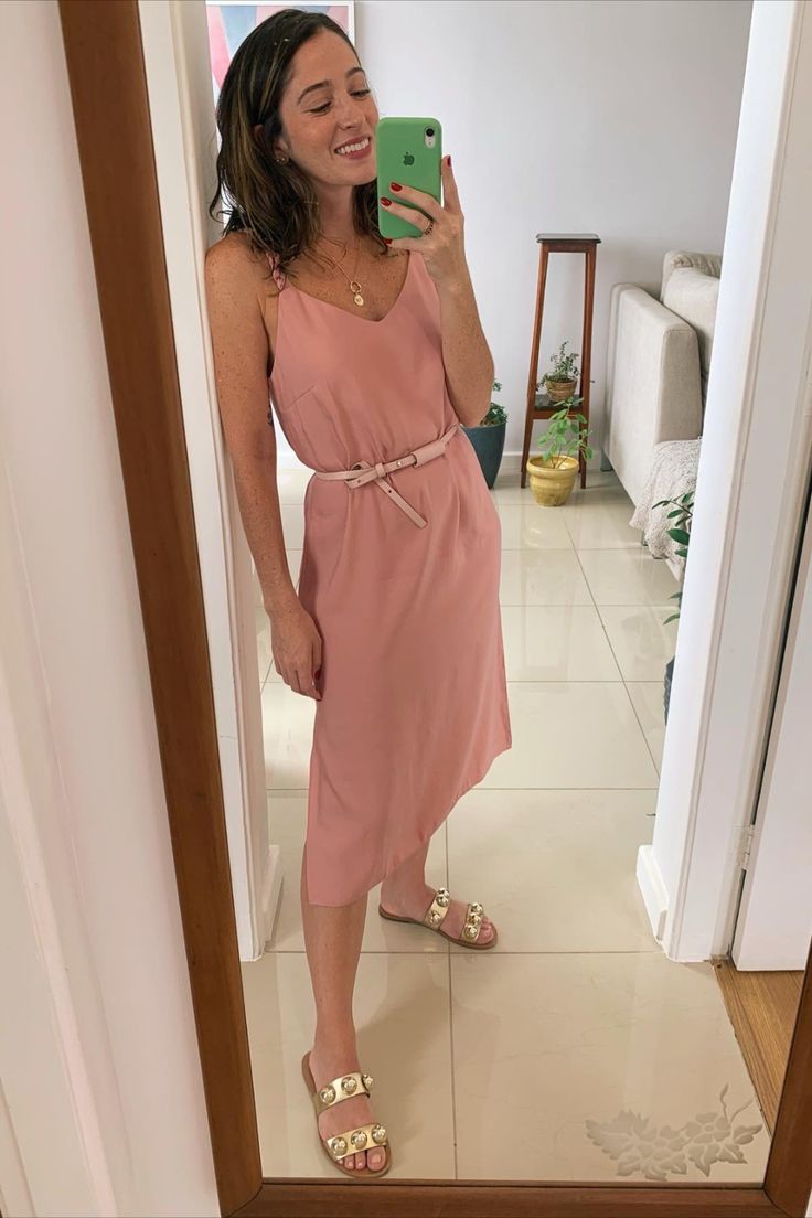 Mulher usando vestido rosa com cinto fino e sandálias douradas.
