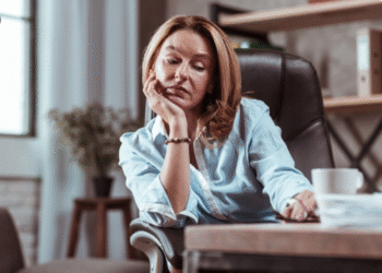 Mulher exausta apoiada na mesa com expressão de cansaço