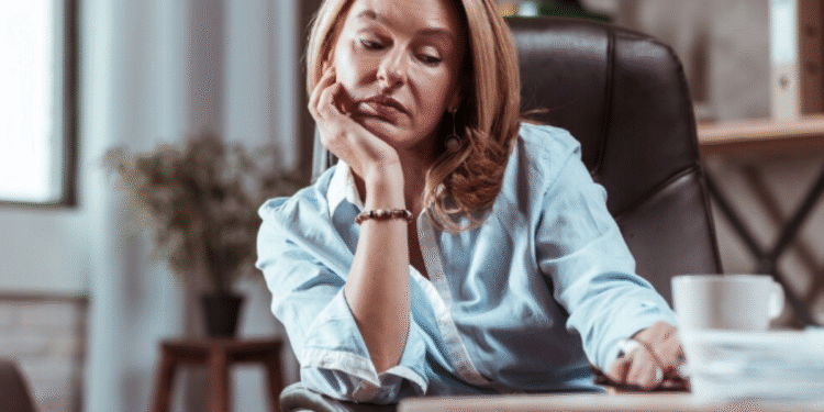 Mulher exausta apoiada na mesa com expressão de cansaço