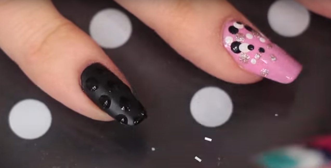 Unhas decoradas com acabamento fosco e bolinhas brilhantes em preto e rosa.
