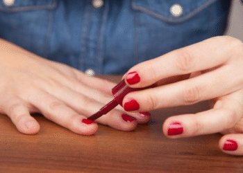 Pessoa aplicando esmalte vermelho nas unhas de forma simples e cuidadosa.