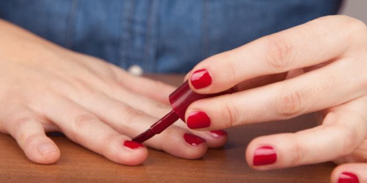 Pessoa aplicando esmalte vermelho nas unhas de forma simples e cuidadosa.