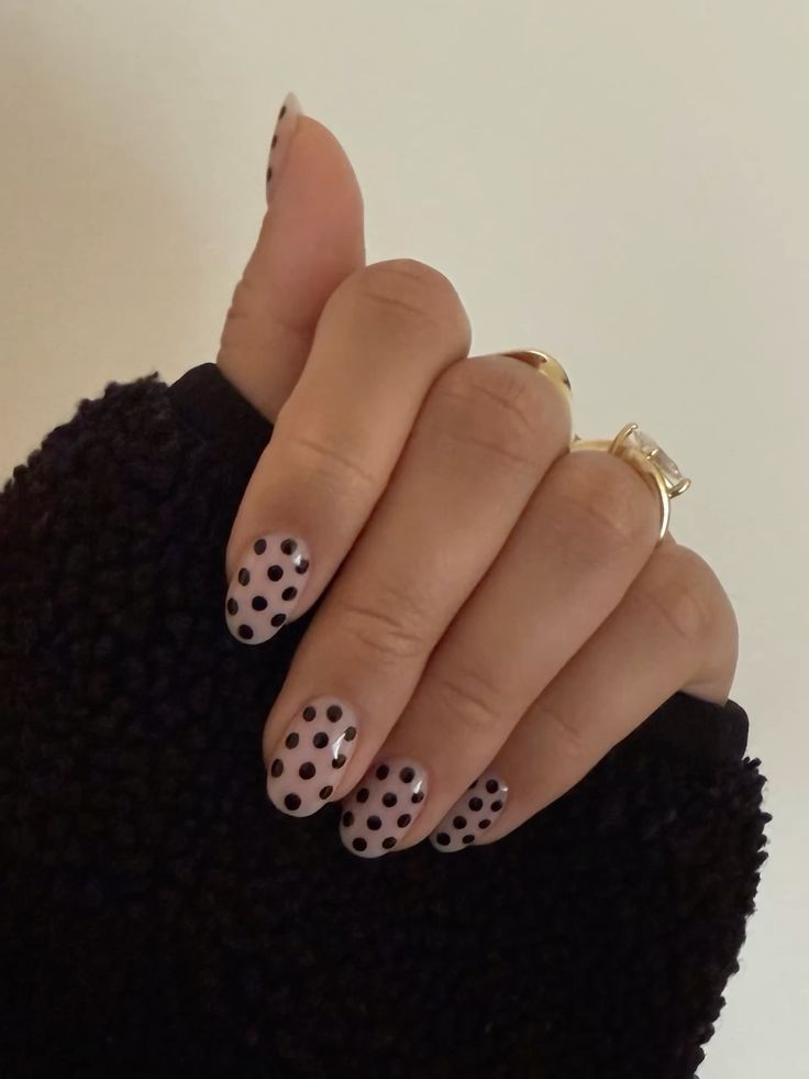 Unhas curtas decoradas com bolinhas pretas sobre esmalte nude.
