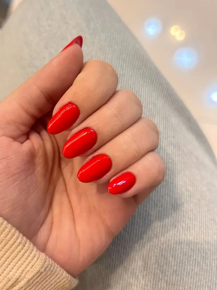 Unhas vermelhas estilo tomate com formato oval, brilhantes e bem cuidadas.