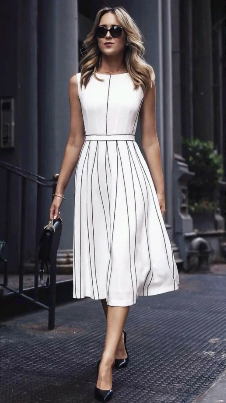 Mulher usando vestido evasê branco com listras, adequado para corpo triângulo, destacando a cintura e equilibrando os quadris.