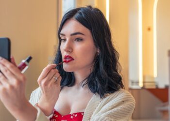 Mulher aplicando batom vermelho enquanto se olha no celular