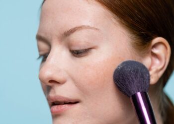 Mulher aplicando blush no rosto, enfatizando um visual natural e fresco.