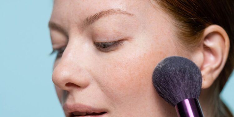 Mulher aplicando blush no rosto, enfatizando um visual natural e fresco.