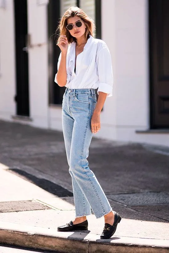 Mulher usando jeans reto com camisa branca, óculos de sol e mocassim preto, destacando a praticidade e estilo do look.
