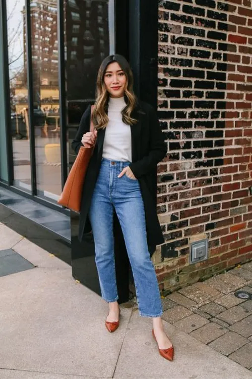Mulher usando sapato de bico fino, com calça jeans e casaco longo, combinando com o estilo elegante para baixinhas.