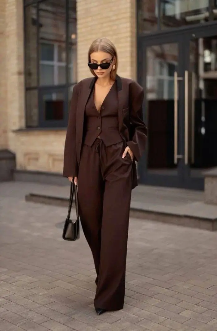 Look elegante em tom marrom com terno e calça ampla, complementado com óculos escuros e bolsa pequena.