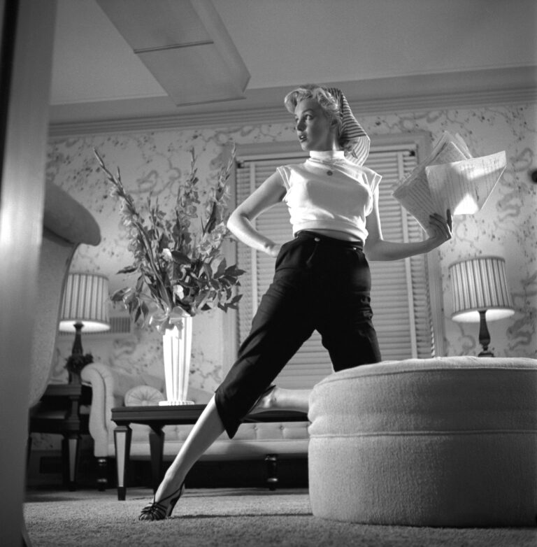 Marilyn Monroe posa com calça capri e camiseta branca, acessorizada com um lenço na cabeça.