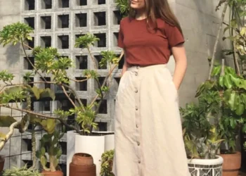 Mulher com saia midi bege e tênis brancos em ambiente casual, mostrando um look moderno e confortável.