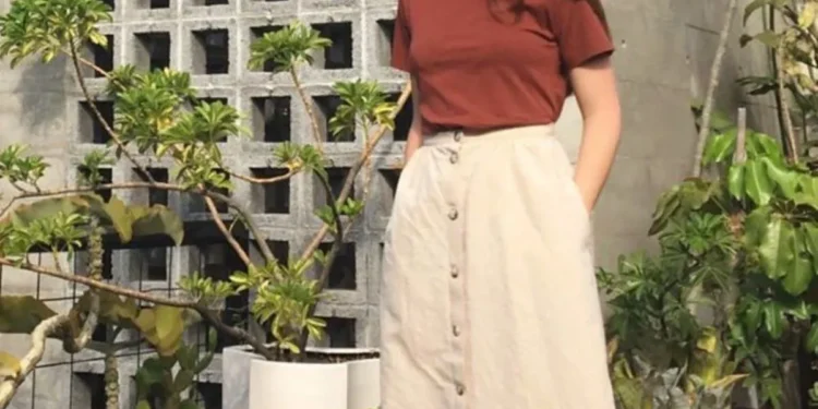 Dica do dia! Saia midi: como usar sem parecer “fora de moda” 1 Mulher com saia midi bege e tênis brancos em ambiente casual, mostrando um look moderno e confortável.