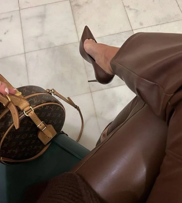 Sapatos de salto fino e bolsa em couro marrom com detalhes em dourado, refletindo luz, proporcionando leveza ao visual.