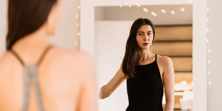 Como se sentir linda mesmo nos dias ruins (vale tentar hoje) 1 Como se sentir linda em qualquer momento, mesmo nos dias difíceis. Mulher refletindo no espelho com um vestido preto, simbolizando autoestima e confiança.
