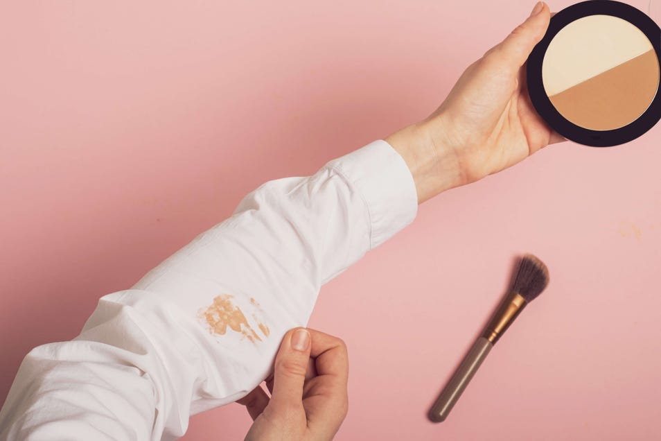 mancha de base em camisa branca com produto de maquiagem ao lado