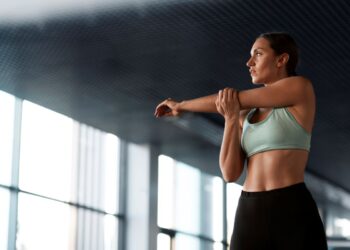Mulher fazendo alongamento em ambiente de treino, usando top esportivo verde