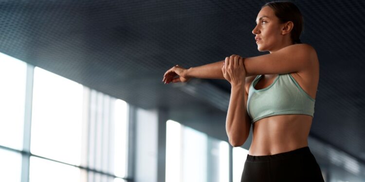 Mulher fazendo alongamento em ambiente de treino, usando top esportivo verde
