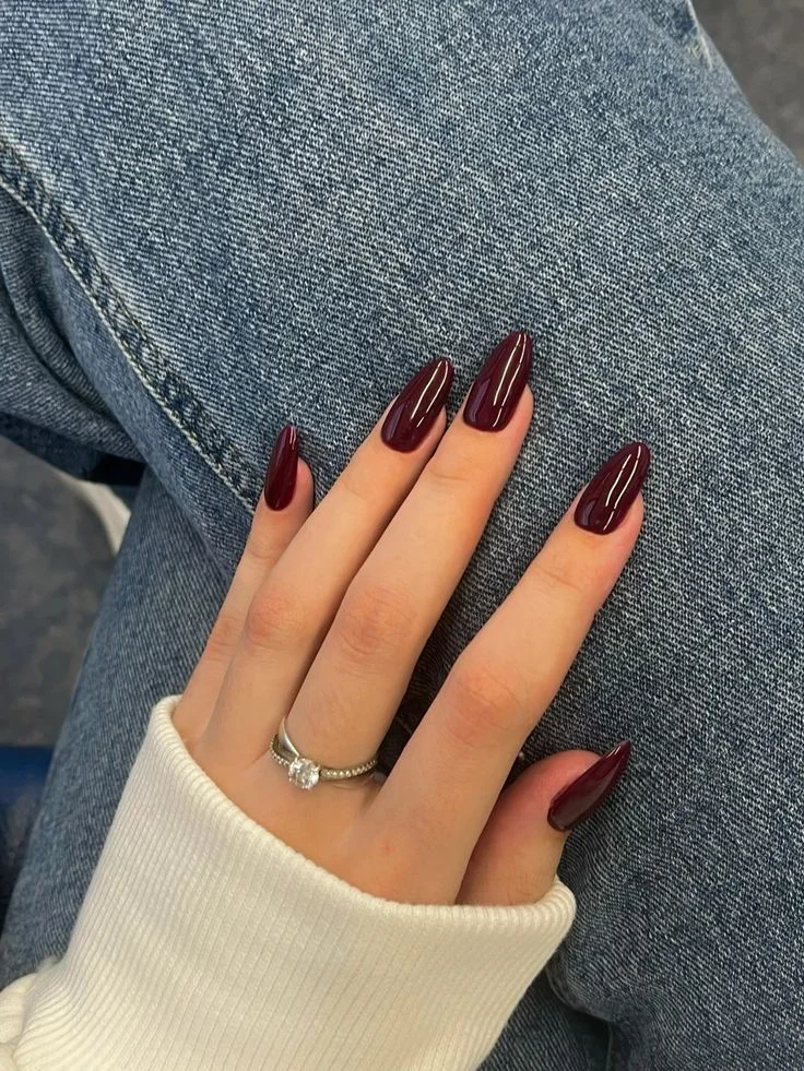 Imagem de unha pintada com esmalte vermelho escuro, no estilo amendoado, com acabamento brilhante e elegante.