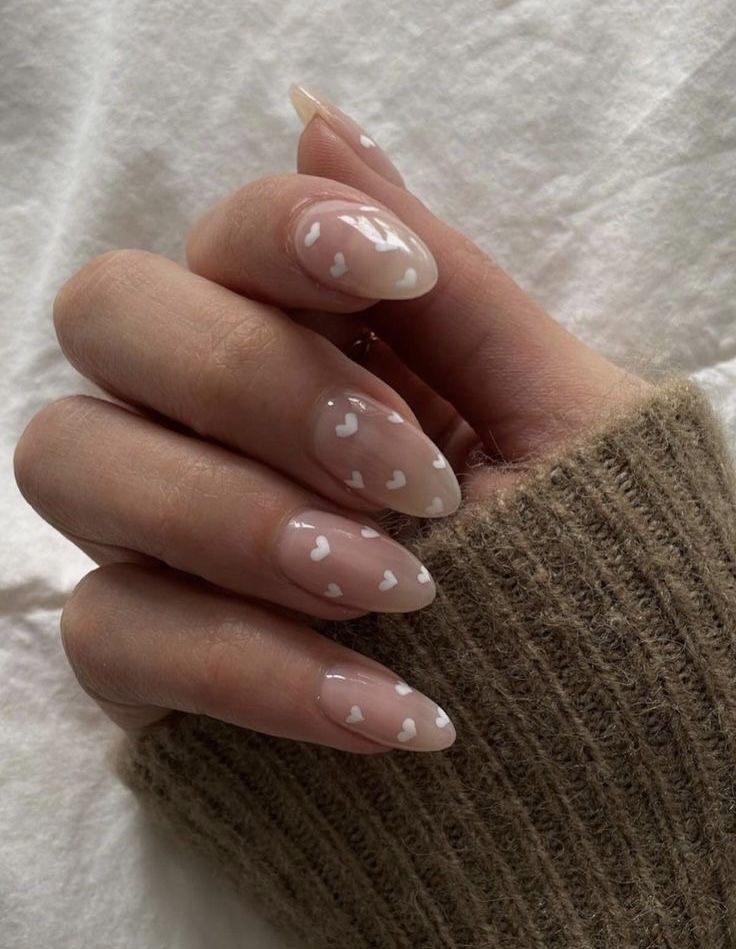Unhas decoradas com esmalte transparente e corações brancos.