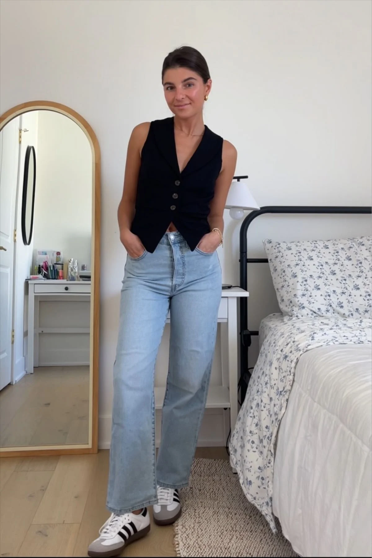 Imagem de uma pessoa usando Adidas Samba com calça jeans clara e blusa preta, em um ambiente interno