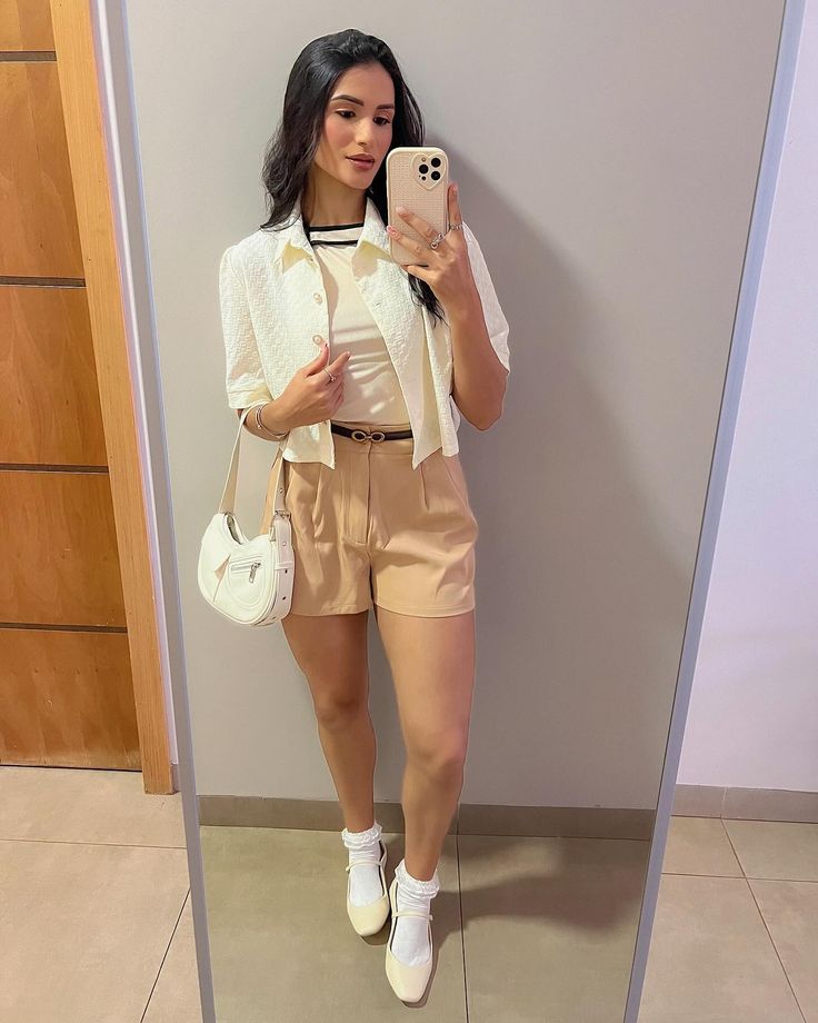 Mulher vestindo look casual com meia de algodão e sapatilha creme, segurando bolsa branca e tirando foto no espelho.