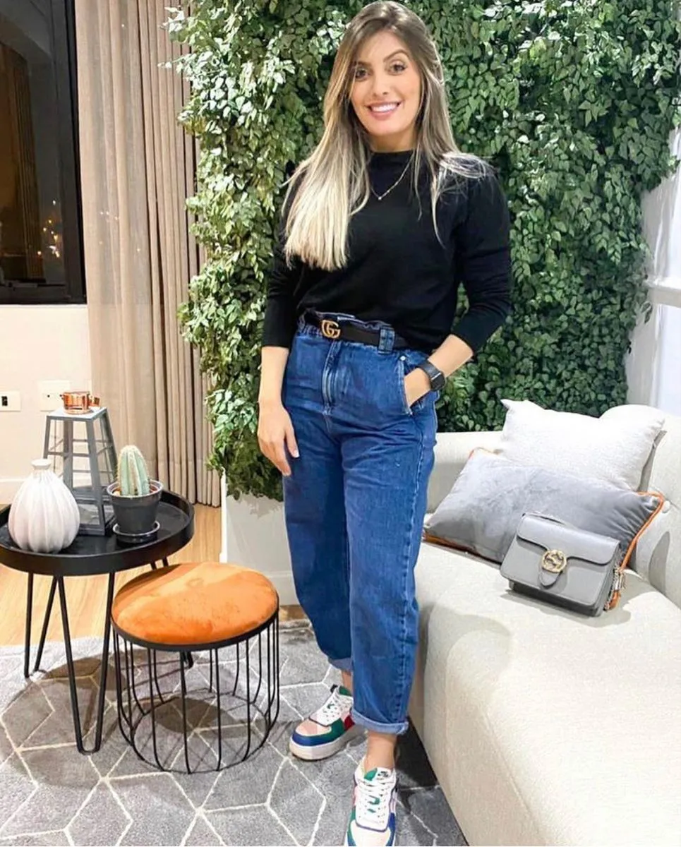Mulher usando Nike Air Force 1, com calça jeans e camiseta preta, em ambiente moderno com decoração verde.