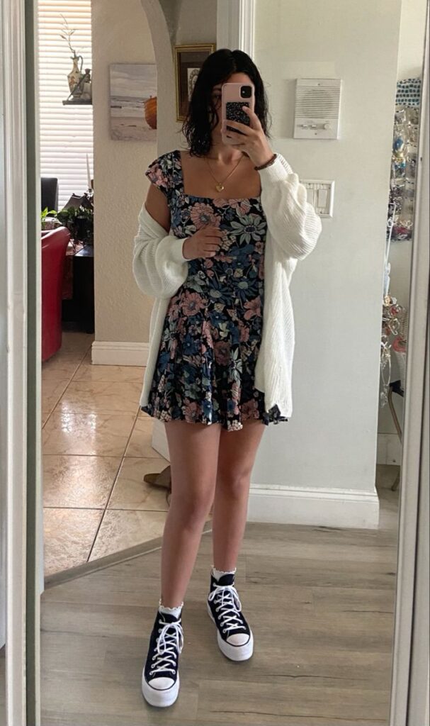 Jovem com vestido florido, cardigan branco e tênis All Star plataforma preto com meias brancas.