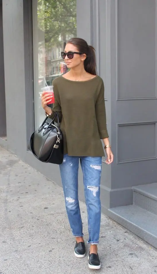 Mulher usando tênis slip-on, calça jeans rasgada e blusa verde, com um copo na mão.