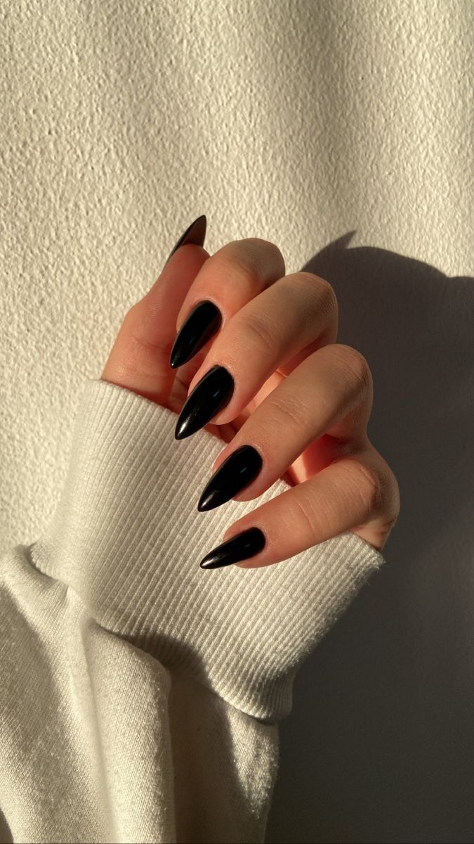 Mão com unhas stiletto esmaltadas na cor preta, com a luz do sol batendo e formando sombras.