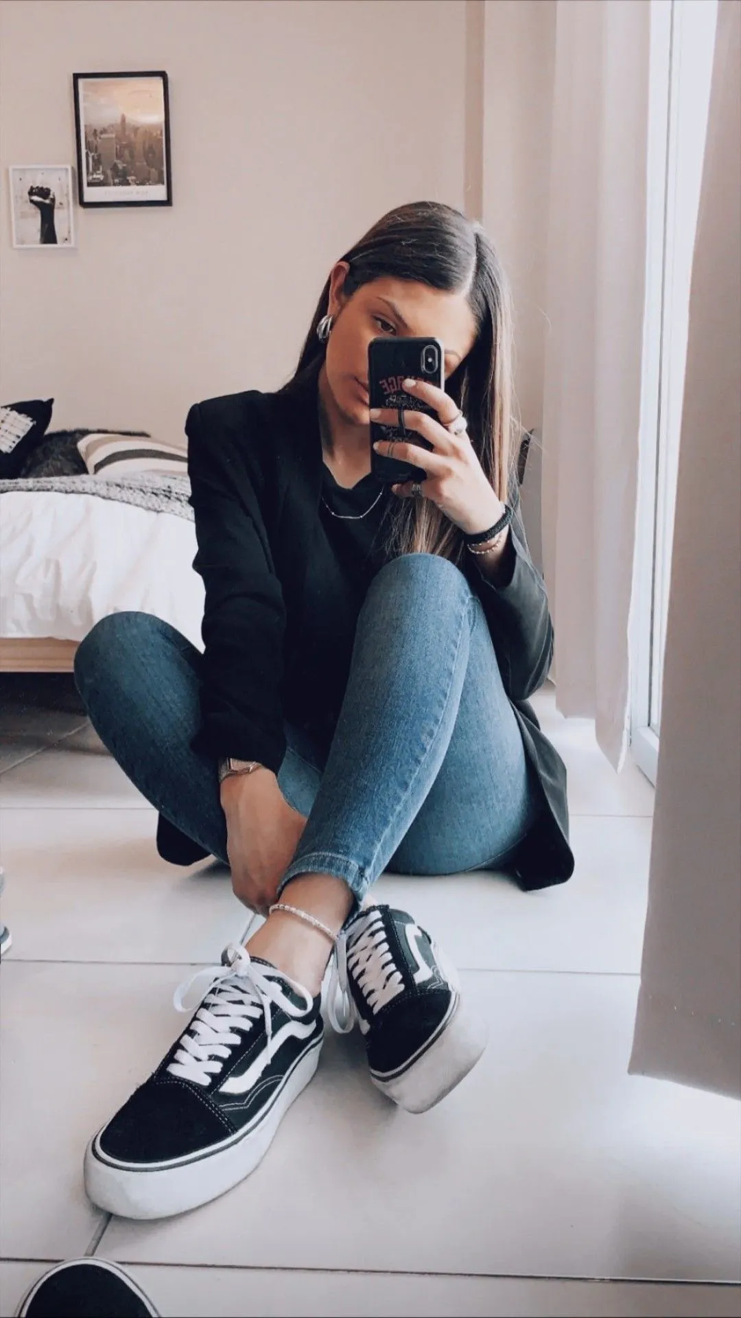 Imagem de um modelo usando Vans Old Skool com jeans azul, posando em um espelho com uma blusa preta e um blazer preto.