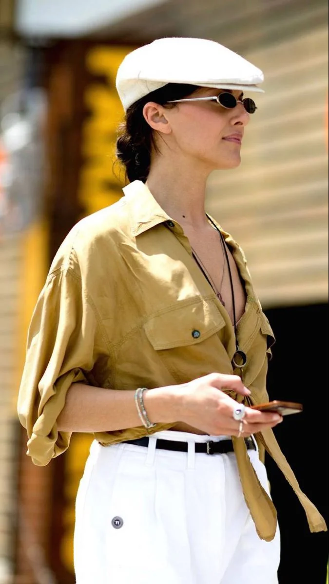 Pessoa com boina branca e óculos escuros, usando uma camisa amarela e calça branca