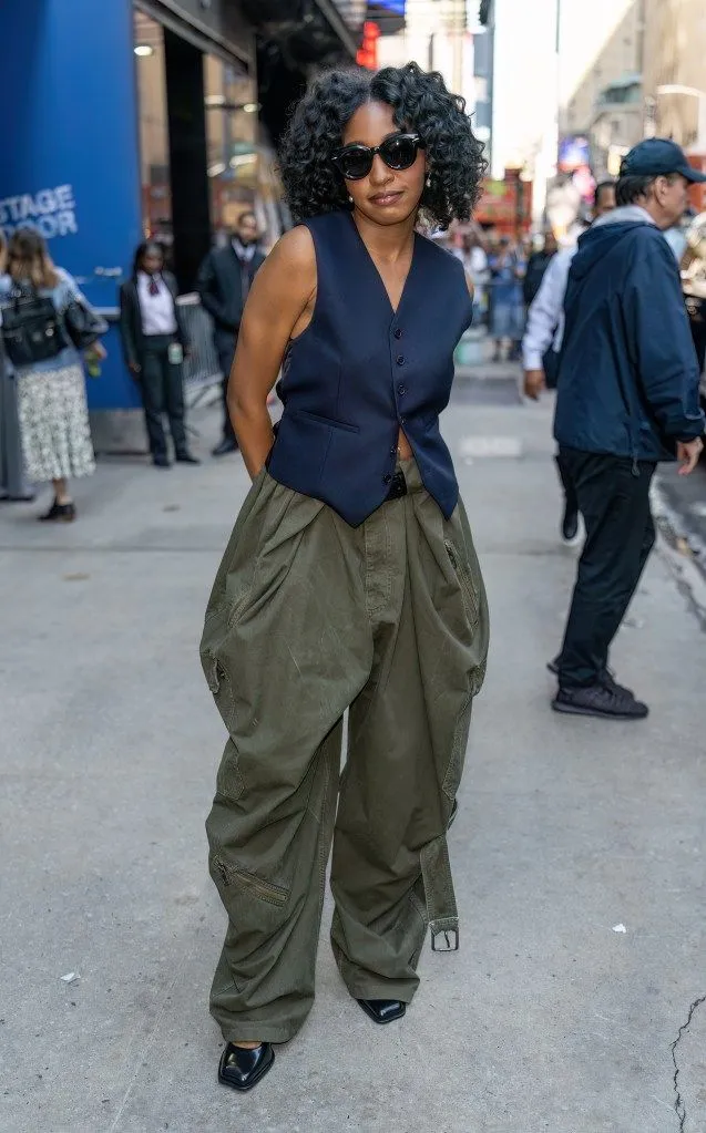 Pessoa usando calça balloon verde com colete escuro e sapatos de bico quadrado, em um estilo urbano e sofisticado.