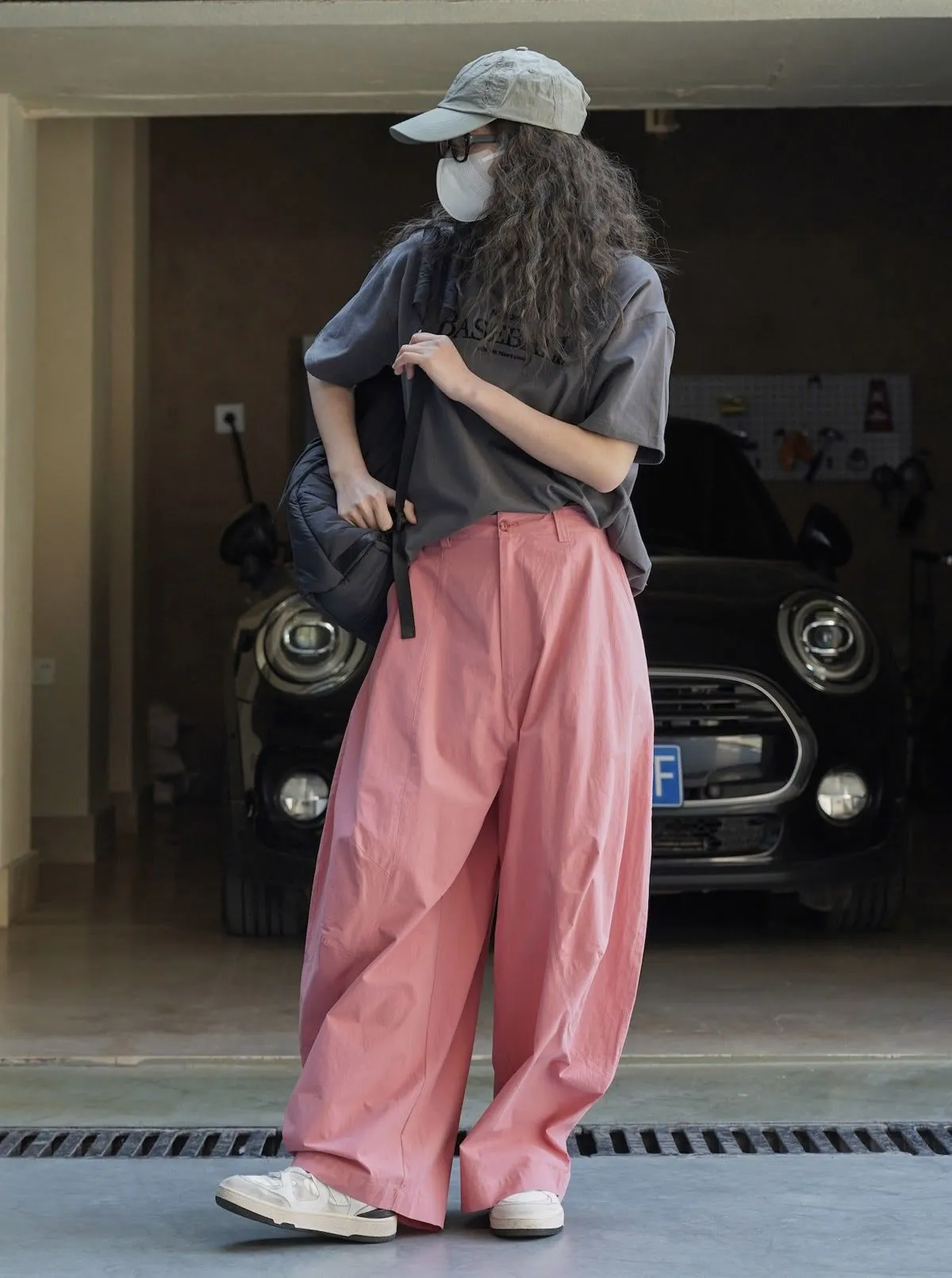 Pessoa usando calça balloon rosa com camiseta ilustrada e tênis branco, em um ambiente descontraído.