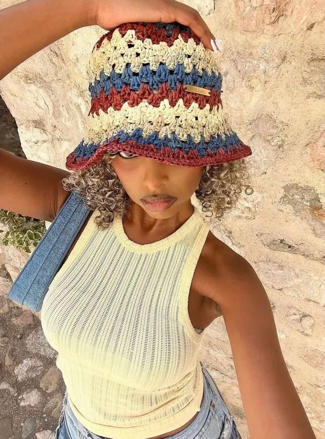 Mulher usando chapéu de crochê colorido com detalhes em vermelho, azul e bege, com blusa amarela e bolsa de jeans