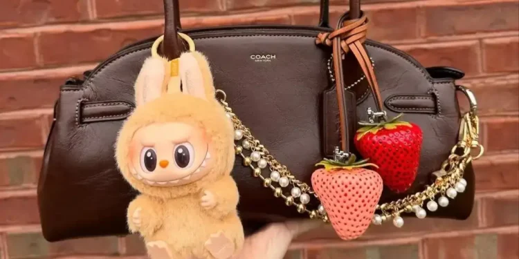 Bolsa marrom Coach decorada com chaveiros divertidos, incluindo morangos e boneco Labubu.