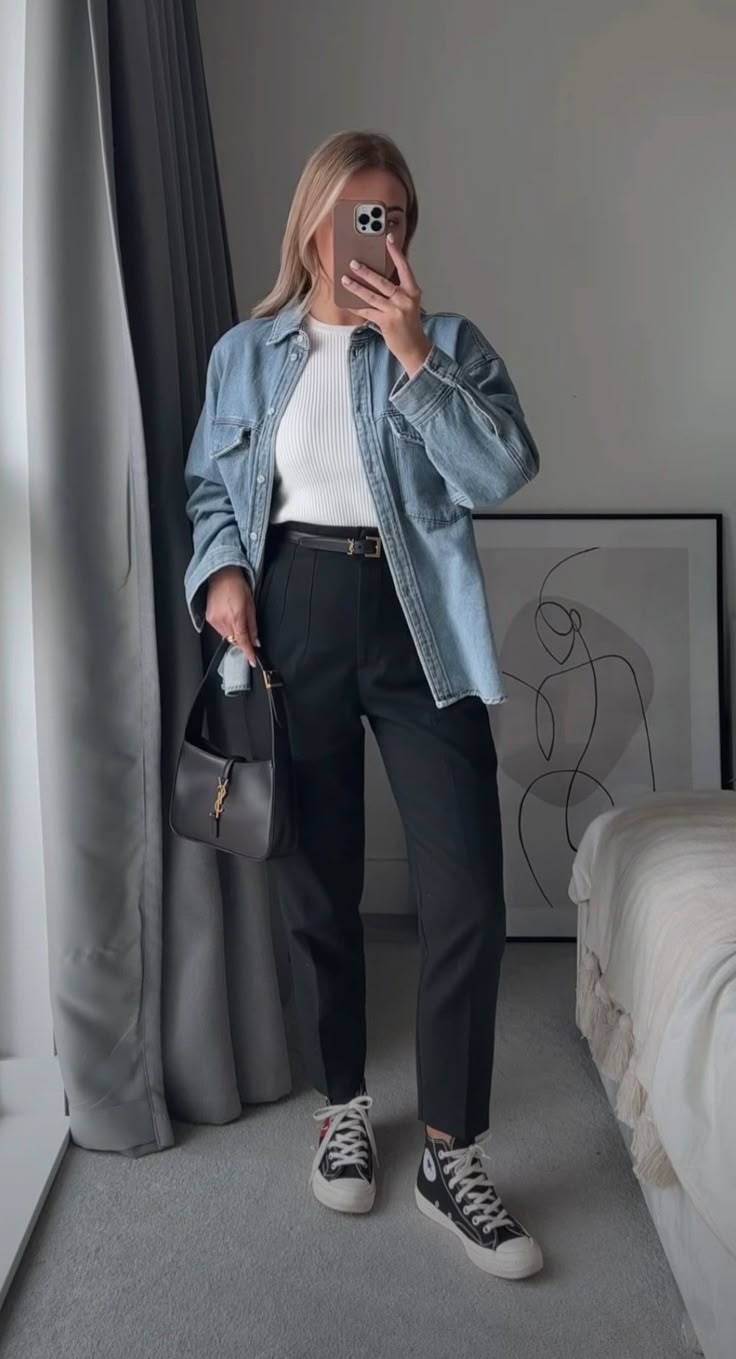 Mulher vestindo calça de alfaiataria preta, camiseta branca canelada, jaqueta jeans oversize e tênis All Star.