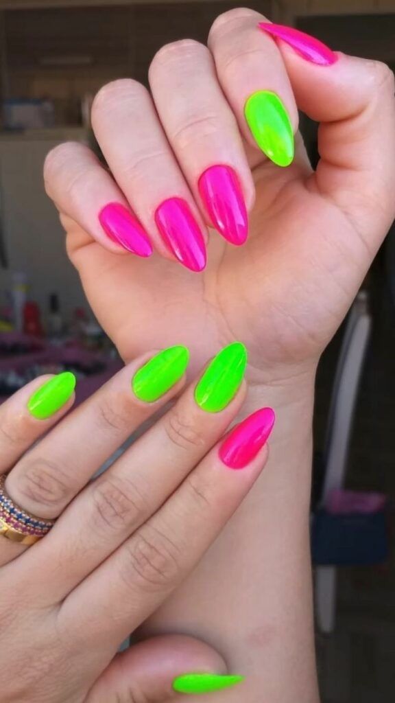 Mãos com unhas alongadas pintadas alternadamente em rosa neon e verde neon.