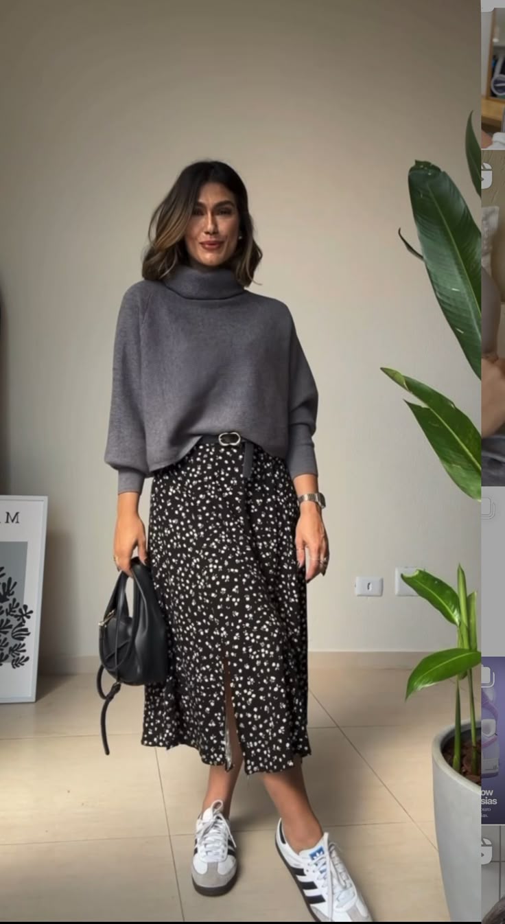 Mulher usando suéter cinza e saia midi floral com tênis branco em look casual e romântico.