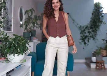 Mulher usando um visual elegante com peças simples: top marrom, calça branca e tênis, em um ambiente moderno e acolhedor.