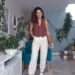 Mulher usando um visual elegante com peças simples: top marrom, calça branca e tênis, em um ambiente moderno e acolhedor.